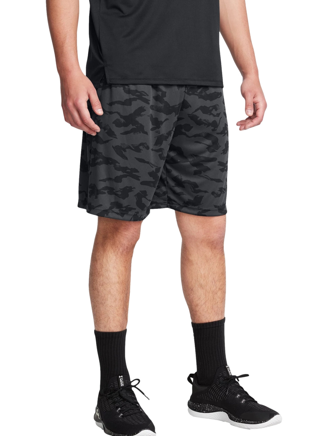 Hombre vistiendo shorts deportivos Under Armour con estampado de camuflaje en tonos negros y grises.