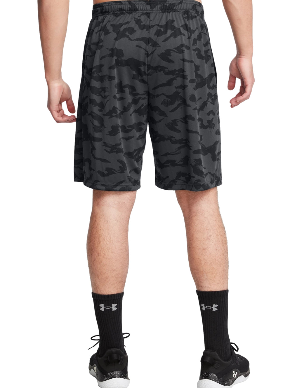 Hombre vistiendo shorts deportivos Under Armour con estampado de camuflaje en tonos negros y grises.