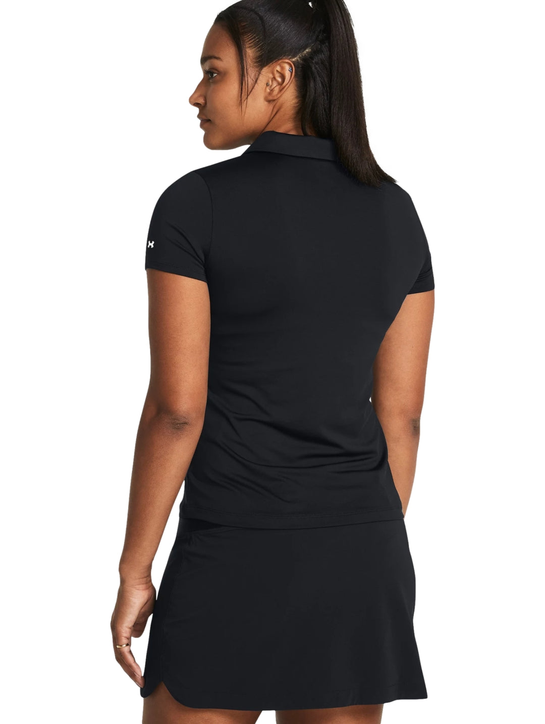 Mujer vistiendo polo deportiva Under Armour de color negro y falda a juego.