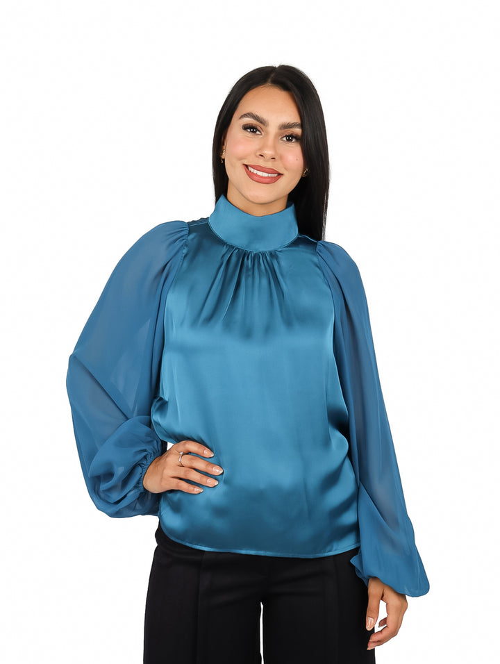 Mujer vistiendo blusa verde satinada de cuello alto y mangas largas abullonadas.