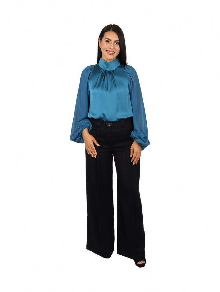 Mujer vistiendo blusa verde satinada de cuello alto y mangas largas abullonadas.