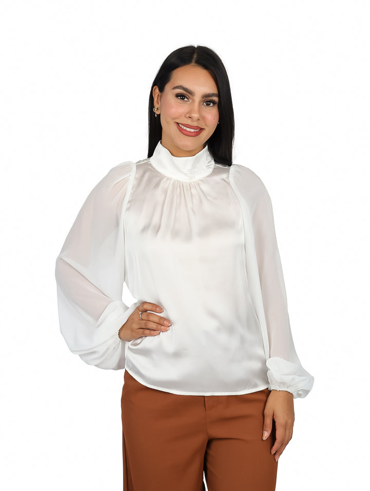 Mujer vistiendo blusa color ivory de cuello alto y mangas largas con acabado brillante.