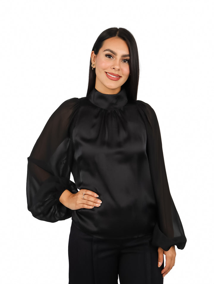 Mujer vistiendo una blusa negra elegante de cuello alto y mangas largas transparentes.