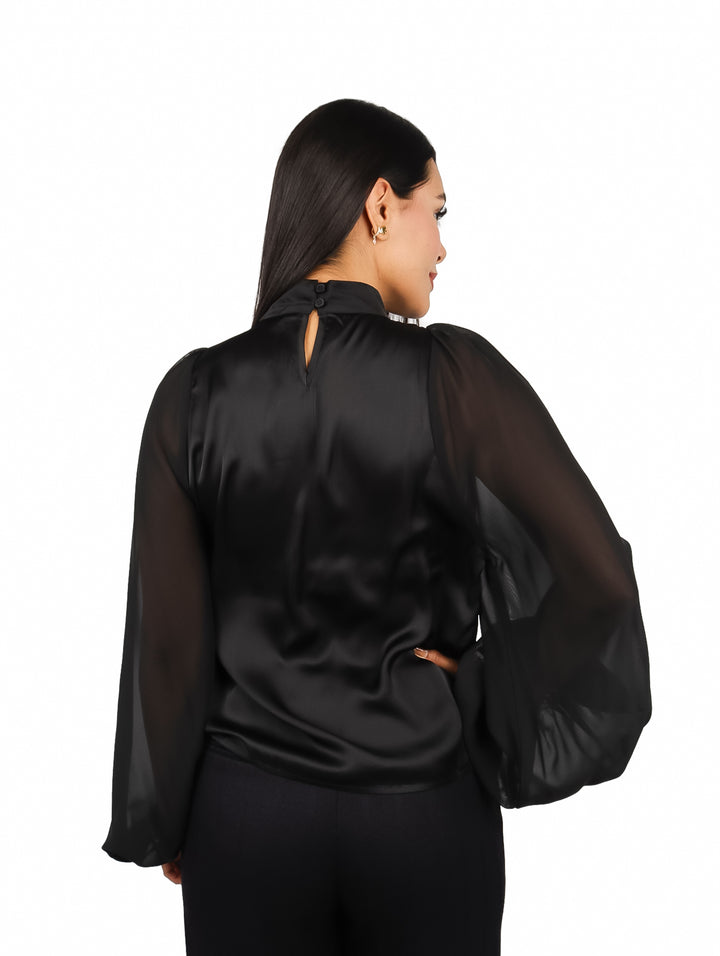 Mujer vistiendo una blusa negra elegante de cuello alto y mangas largas transparentes.