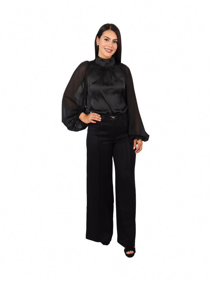 Mujer vistiendo una blusa negra elegante de cuello alto y mangas largas transparentes.