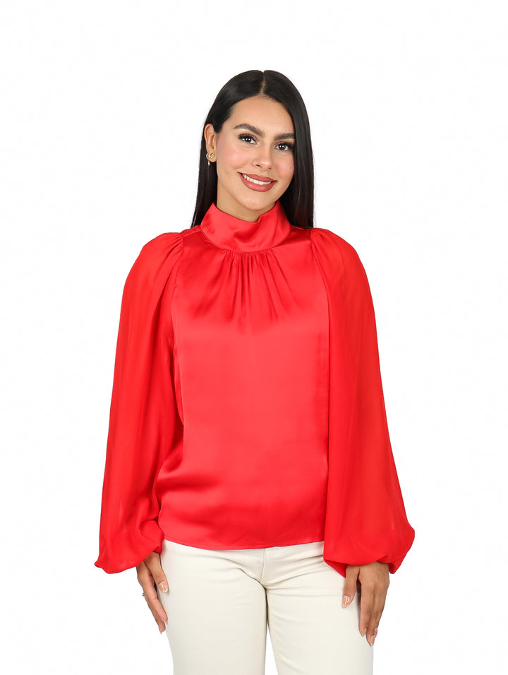 Mujer vistiendo una blusa roja de manga larga y cuello alto sobre fondo blanco.