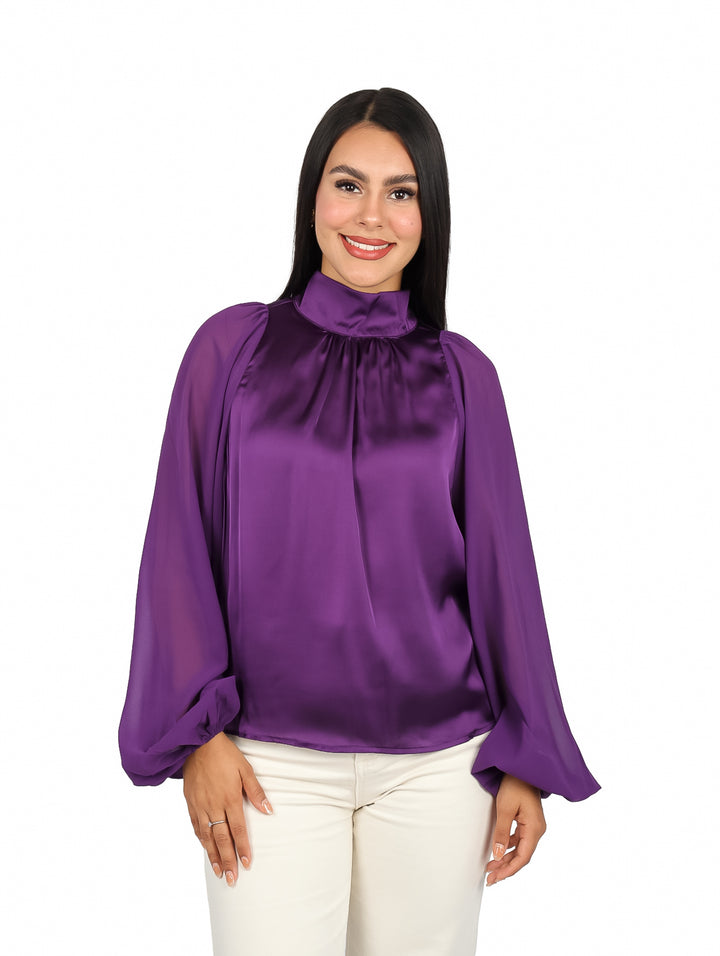 Mujer vistiendo una blusa morada satinada de cuello alto y mangas largas.