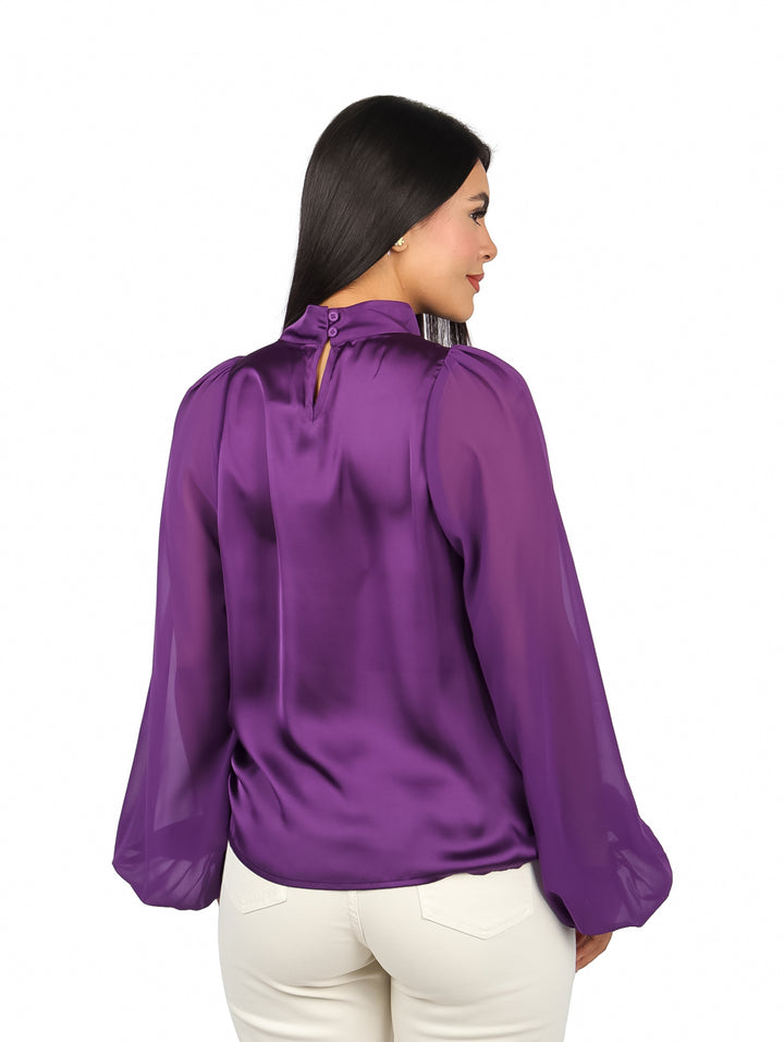 Mujer vistiendo una blusa morada satinada de cuello alto y mangas largas.