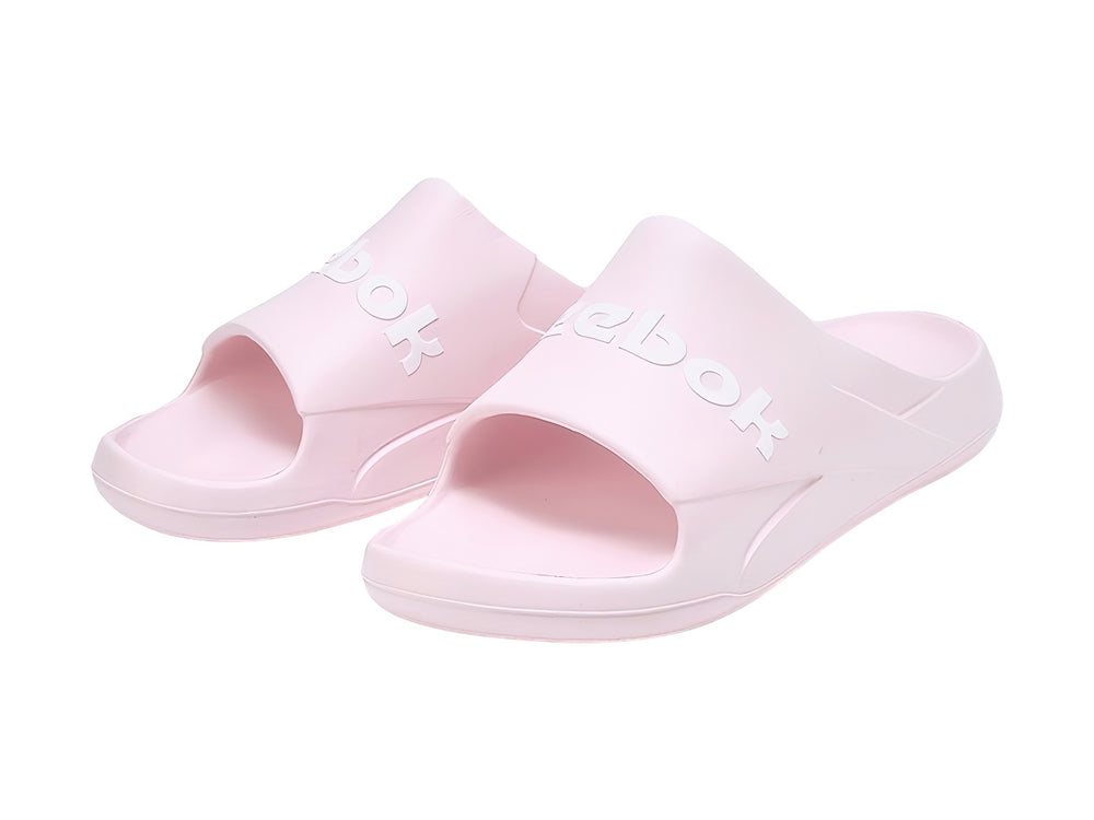 Sandalias slide Reebok en color rosa pálido con logotipo blanco en la banda superior.
