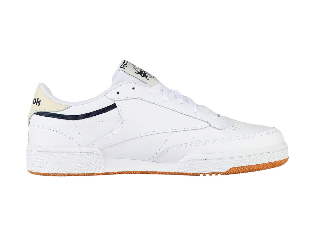 Tenis Reebok Club C 85 color blanco con suela de goma color miel y detalles en azul marino.