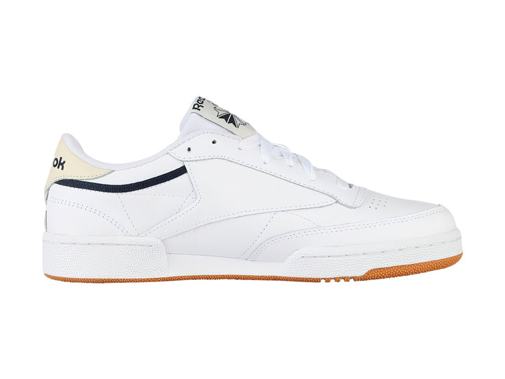 Tenis Reebok Club C 85 color blanco con suela de goma color miel y detalles en azul marino.