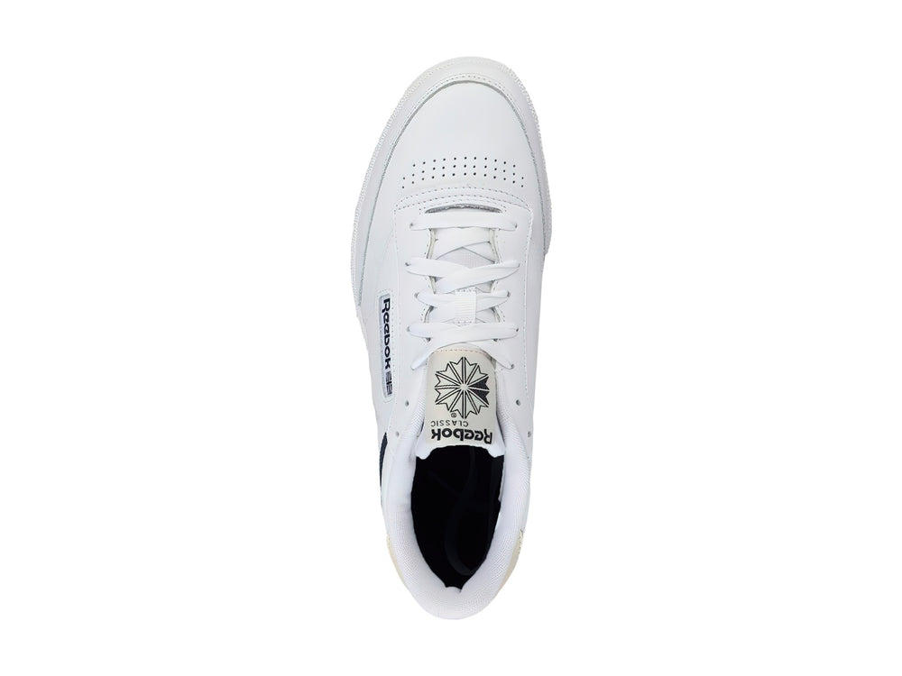 Tenis Reebok Club C 85 color blanco con suela de goma color miel y detalles en azul marino.