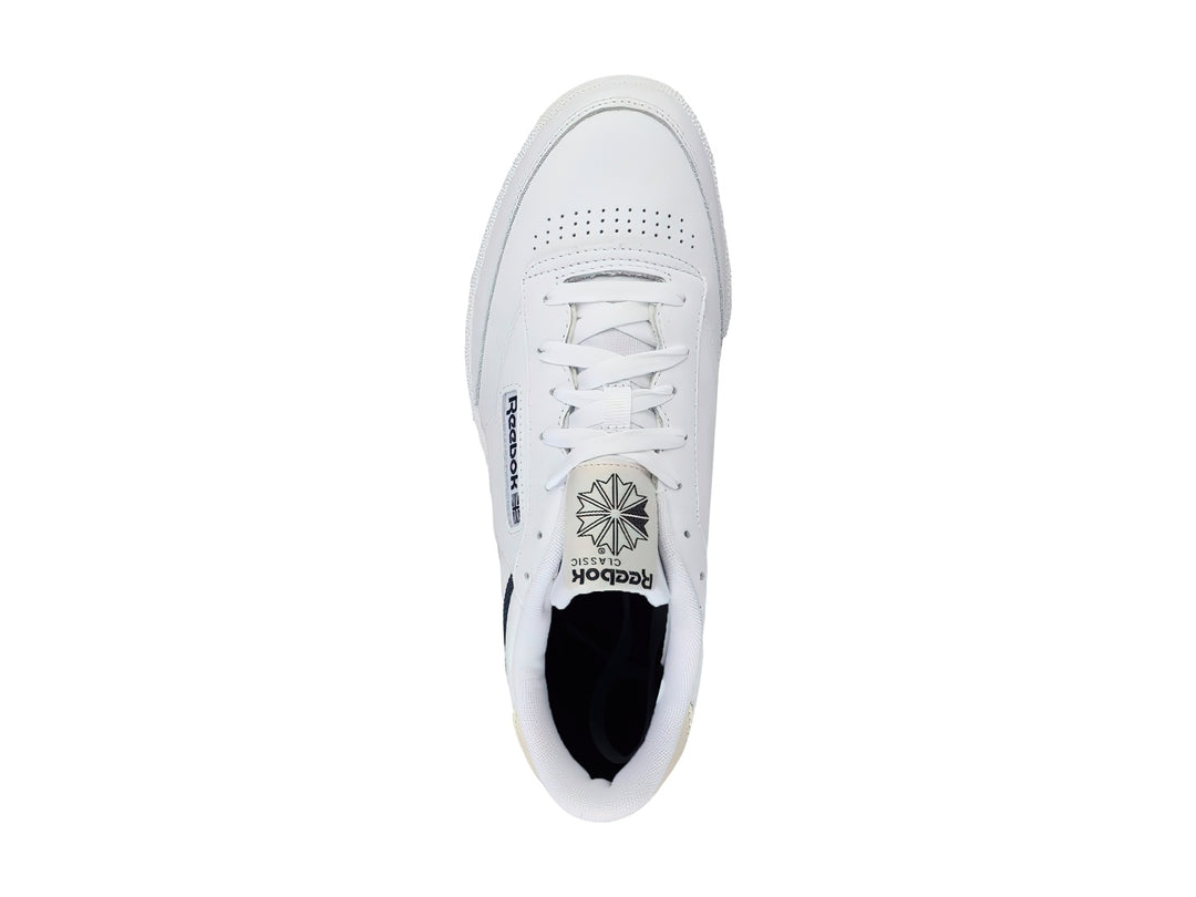 Tenis Reebok Club C 85 color blanco con suela de goma color miel y detalles en azul marino.