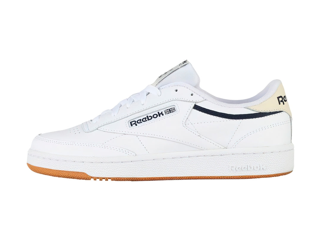 Tenis Reebok Club C 85 color blanco con suela de goma color miel y detalles en azul marino.