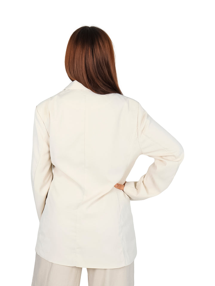 Mujer vistiendo un saco blazer color beige con botones oscuros y pantalones a juego.