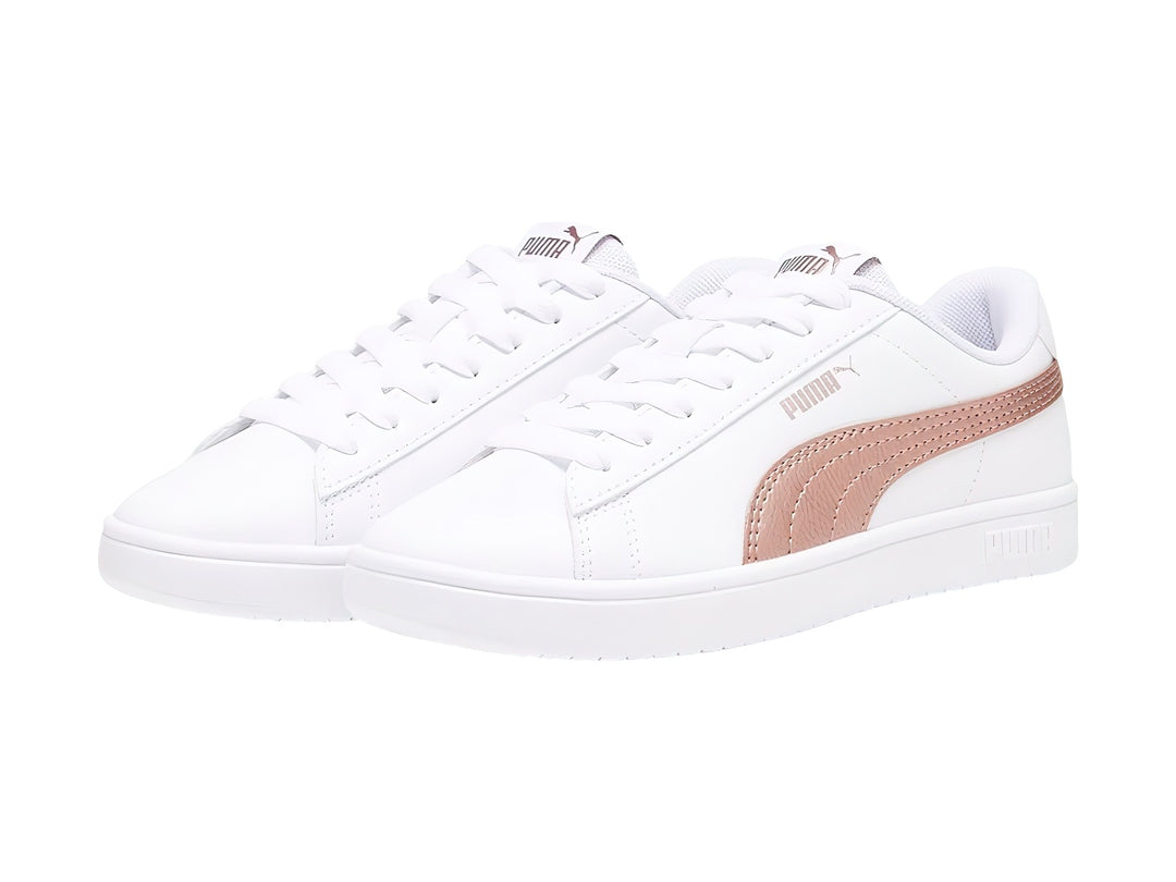 Tenis PUMA Rickie Classic Jr en color blanco con franja lateral en tono oro rosa y suela blanca.