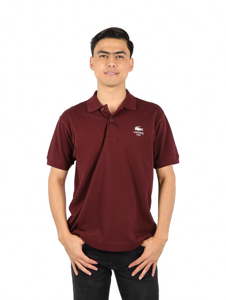 Hombre vistiendo una playera polo Lacoste de color bordeaux con cuello y manga corta.