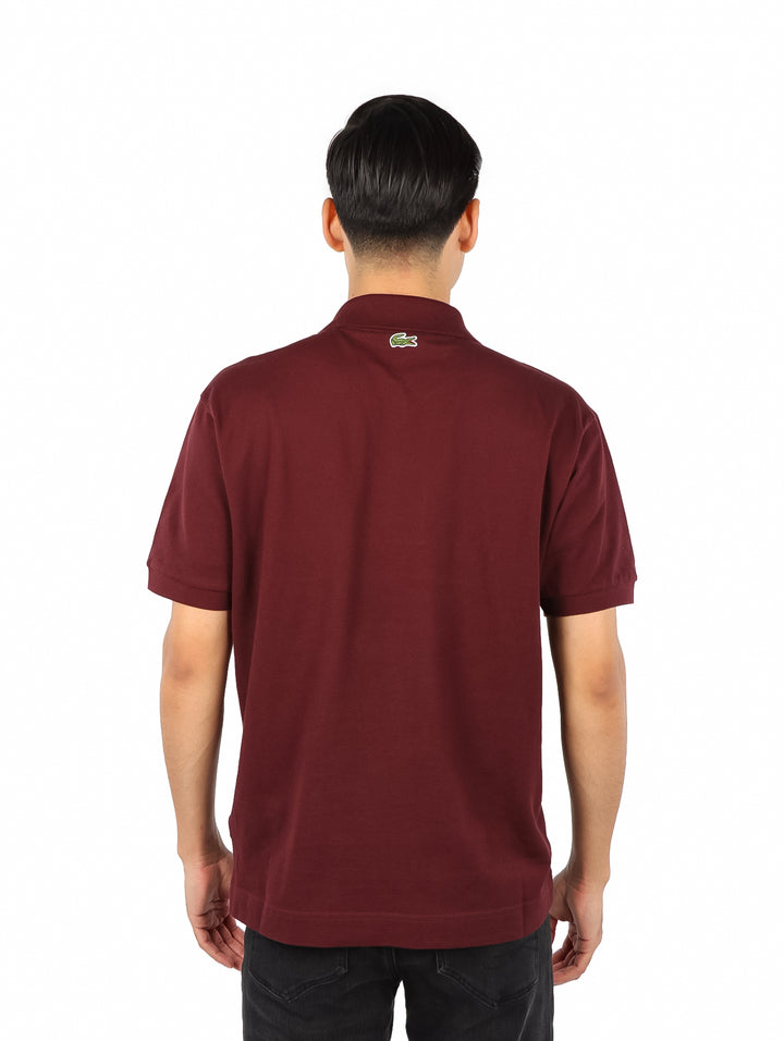 Hombre vistiendo una playera polo Lacoste de color bordeaux con cuello y manga corta.