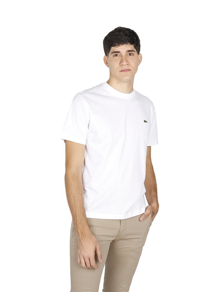 Hombre vistiendo una camiseta blanca de manga corta con cuello redondo de la marca Lacoste.