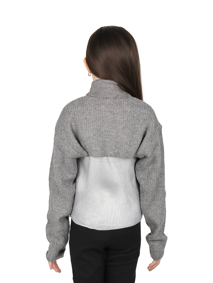 Niña vistiendo blusa de cuello alto en colores gris y plateado con pantalones negros.