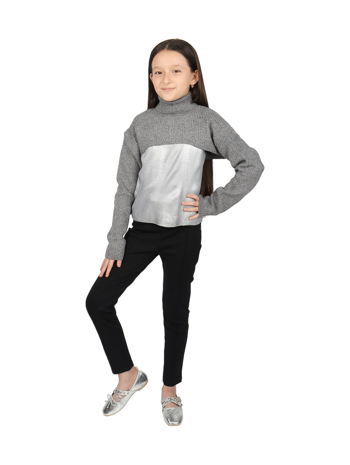 Niña vistiendo blusa de cuello alto en colores gris y plateado con pantalones negros.