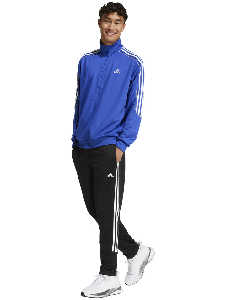Hombre vistiendo conjunto deportivo Adidas con chaqueta azul y pantalón negro con franjas blancas laterales.