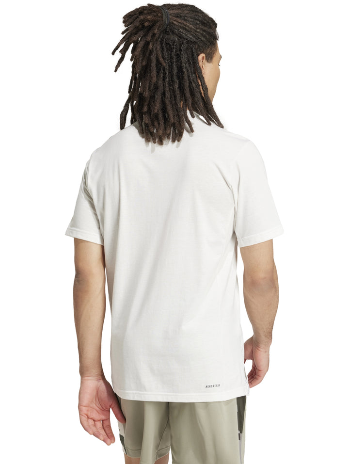 Hombre vistiendo playera blanca Adidas con logo gráfico de camuflaje en el pecho.