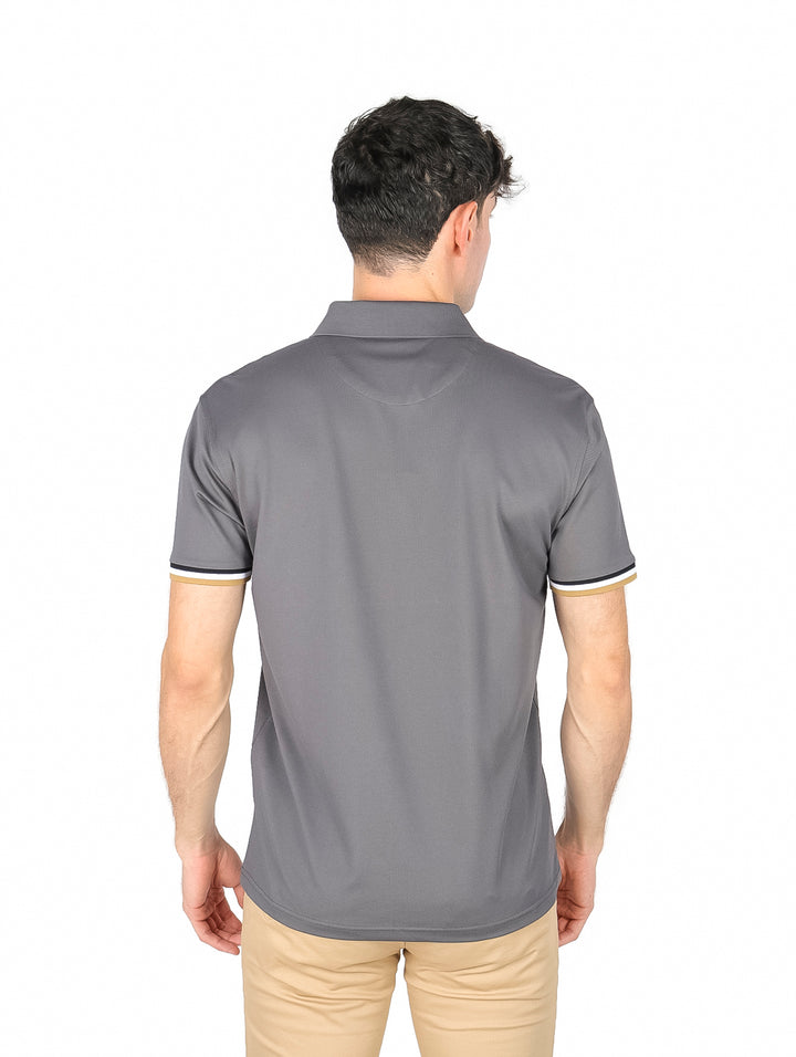 Hombre vistiendo playera polo color charcoal con detalles en blanco y dorado en el cuello y mangas.