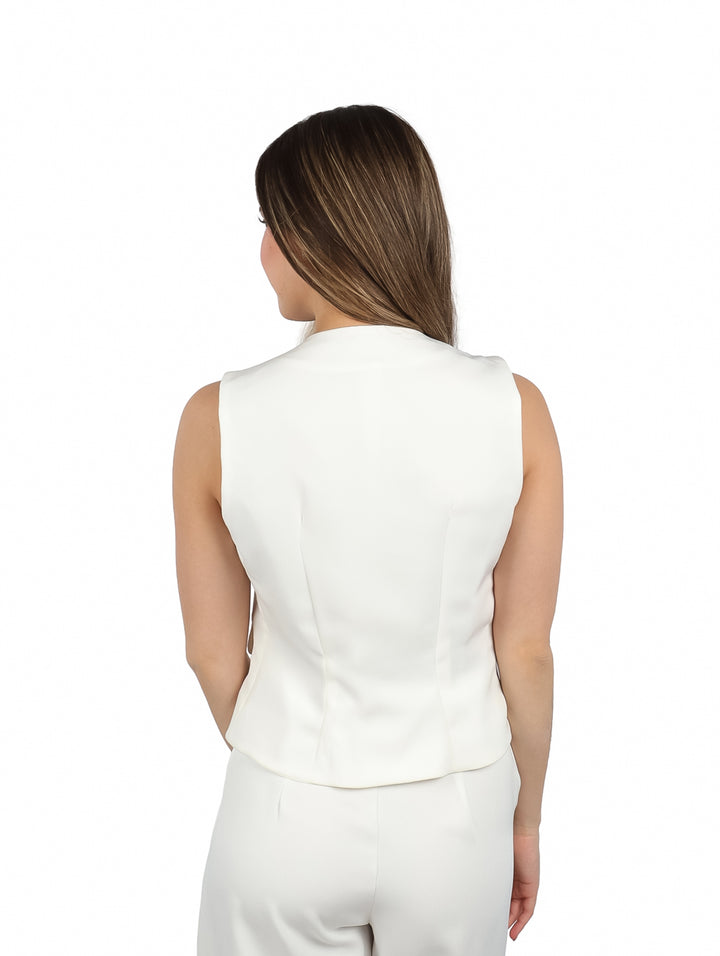 Mujer vistiendo un chaleco color ivory con cinco botones dorados y bolsillos frontales.