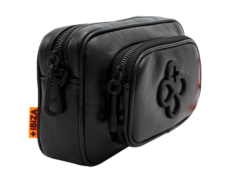 Bolso pequeño de color negro con correa y un accesorio colgante circular en color naranja.