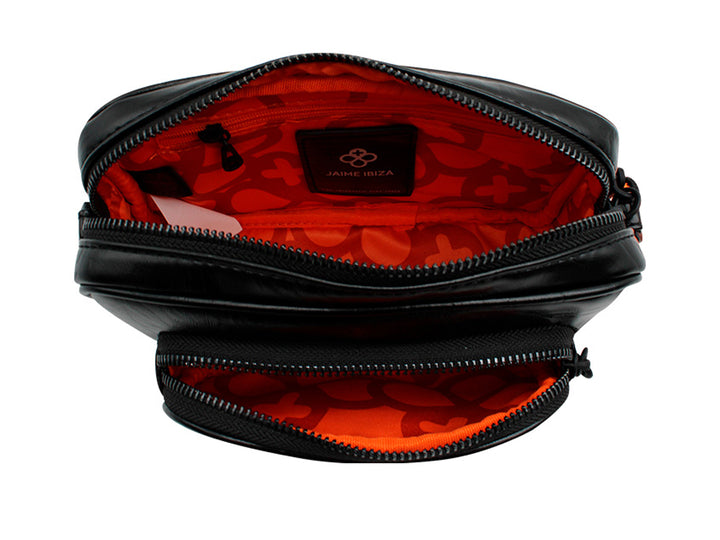 Bolso pequeño de color negro con correa y un accesorio colgante circular en color naranja.