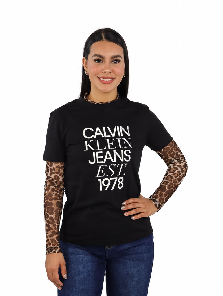 Mujer vistiendo playera negra de manga corta con estampado blanco de Calvin Klein Jeans.