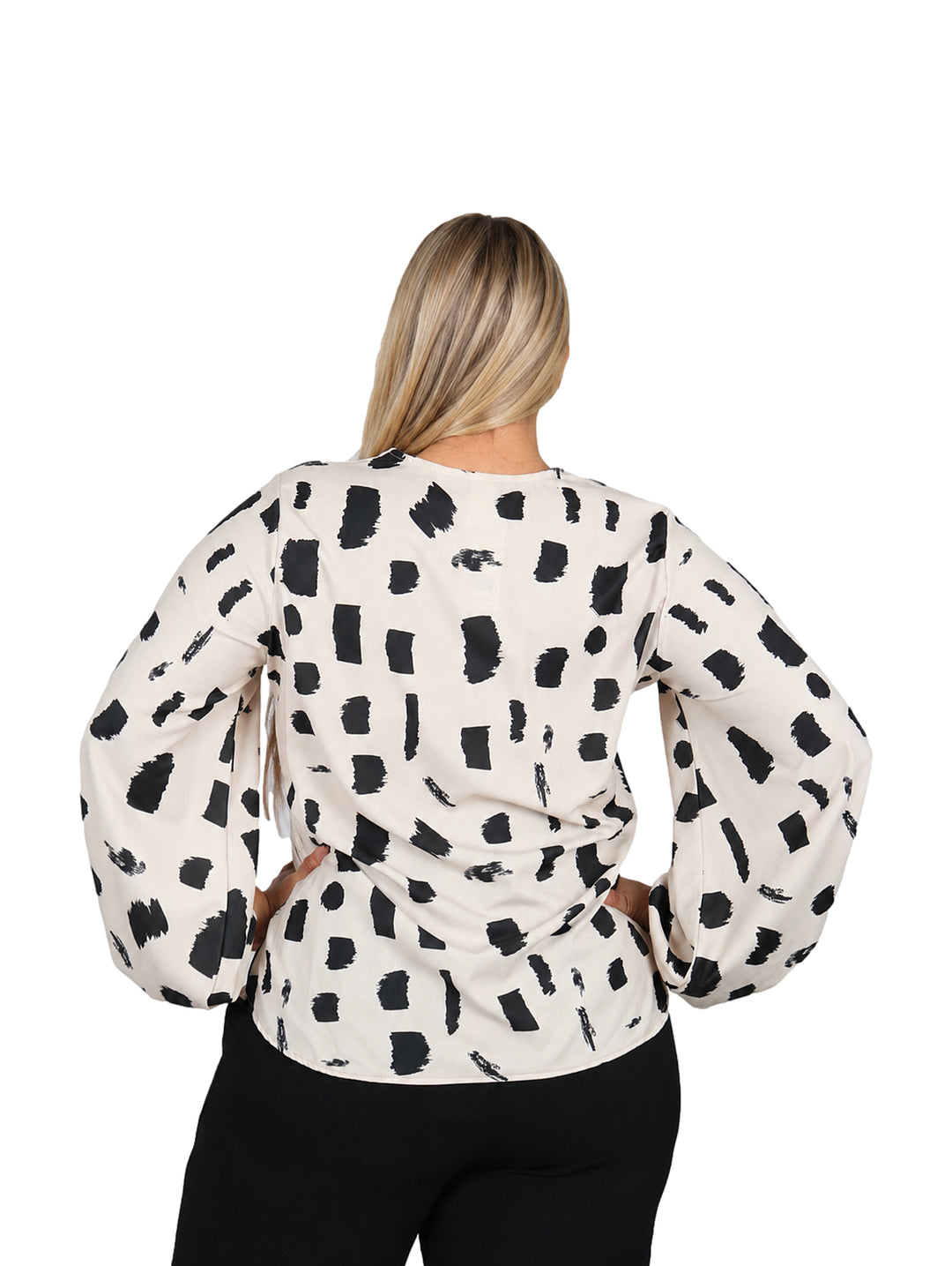 Mujer vistiendo blusa color beige con estampado abstracto negro, cuello en V y mangas largas acampanadas.