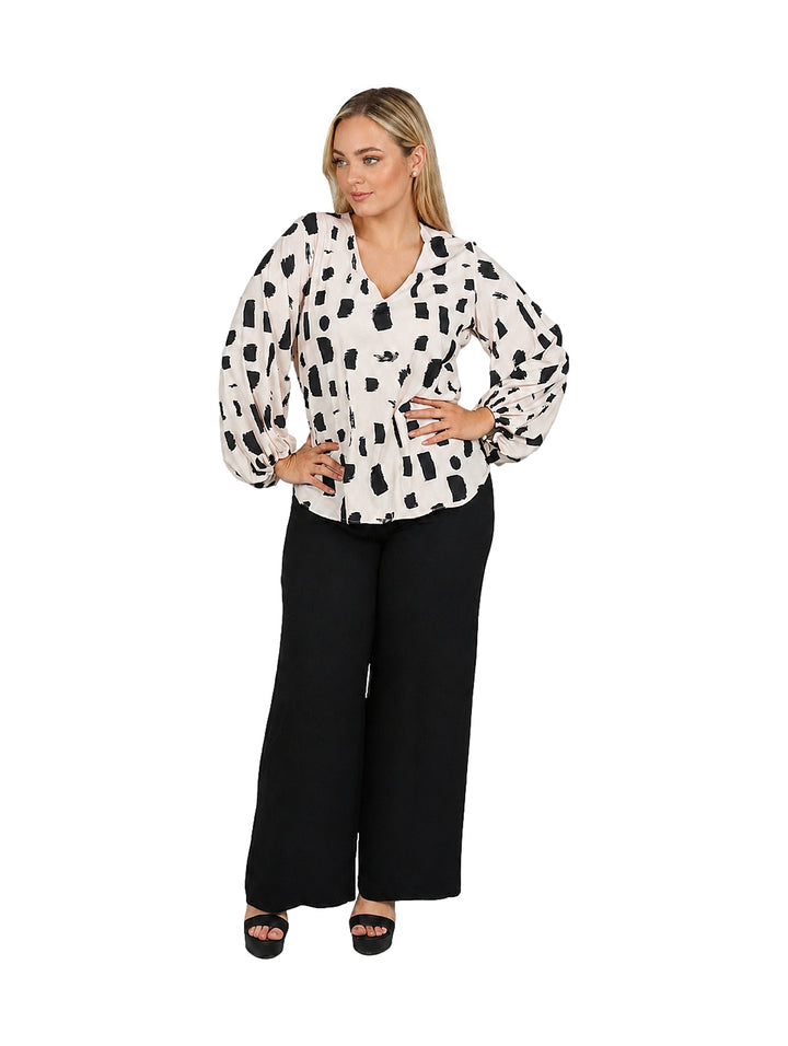 Mujer vistiendo blusa color beige con estampado abstracto negro, cuello en V y mangas largas acampanadas.