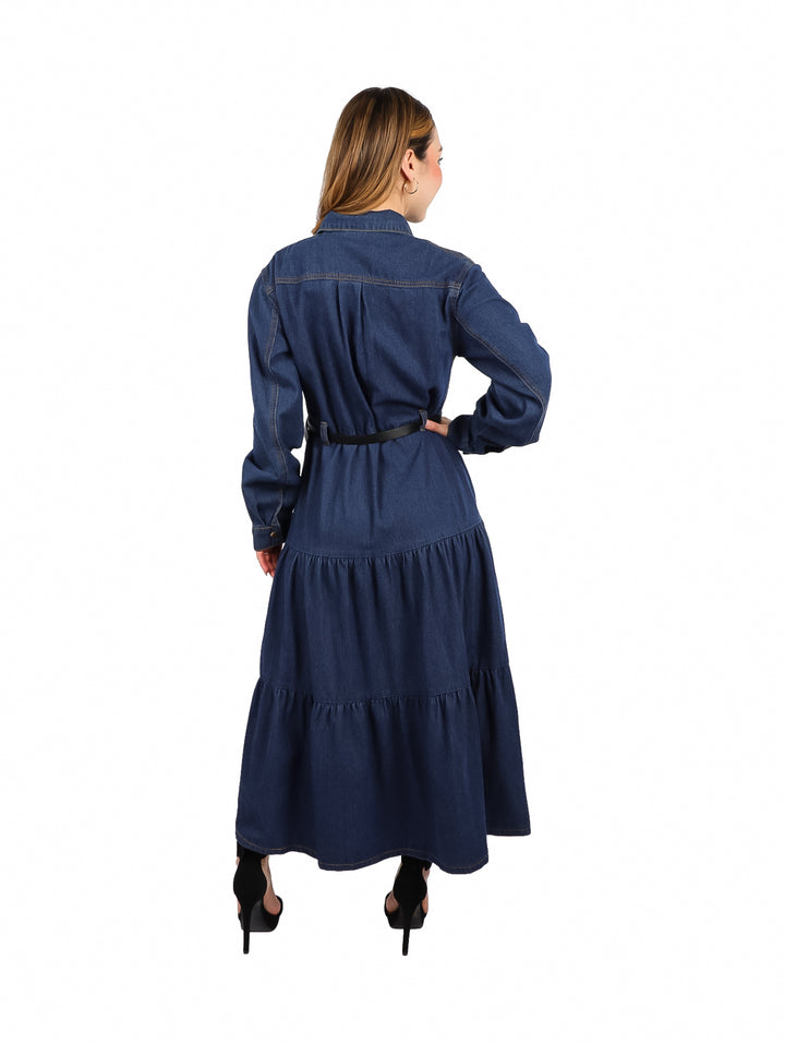 Mujer vistiendo un vestido largo de mezclilla azul oscuro con botones frontales, manga larga y cinturón negro.