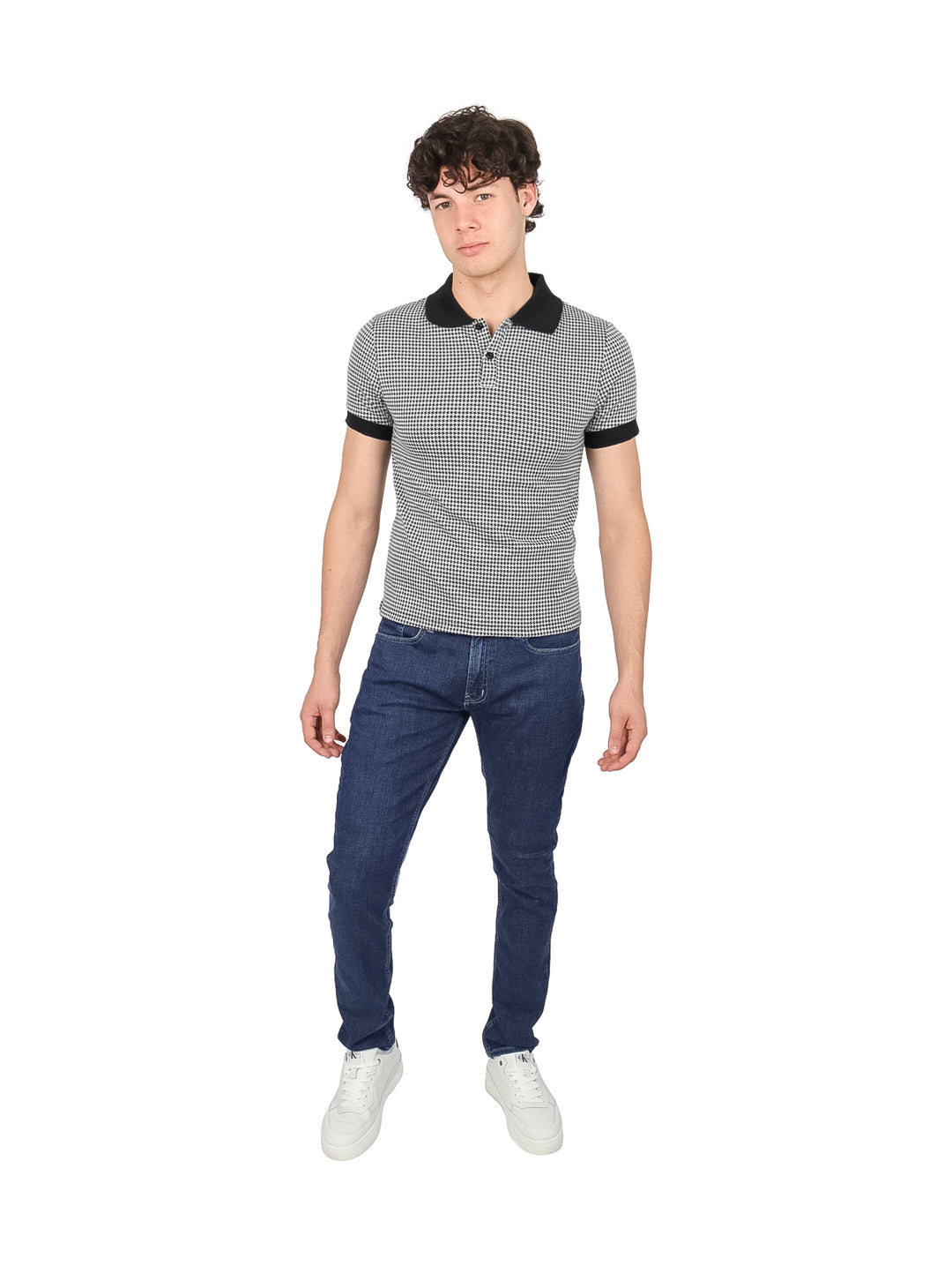 Hombre vistiendo camiseta tipo polo con estampado de cuadros pequeños en blanco y negro y cuello sólido negro.