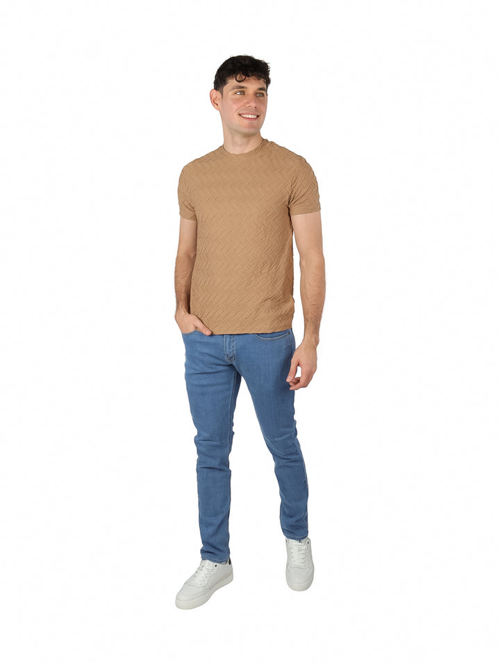 Hombre vistiendo playera de manga corta color marrón con textura geométrica en relieve y jeans azules.