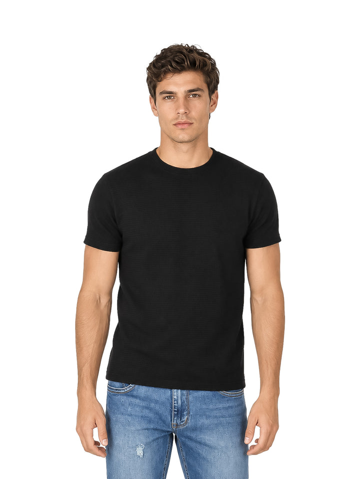 Hombre vistiendo una playera negra de manga corta con textura y pantalones de mezclilla azules.