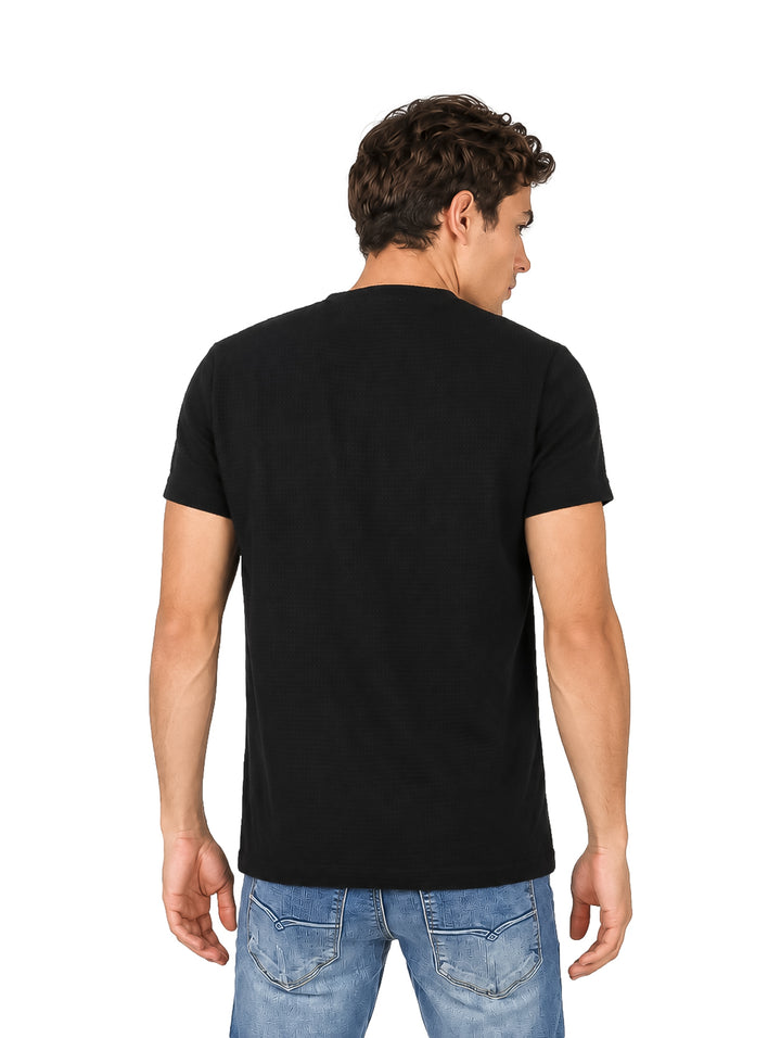 Hombre vistiendo una playera negra de manga corta con textura y pantalones de mezclilla azules.