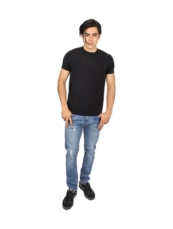Hombre vistiendo una playera negra de manga corta con textura y pantalones de mezclilla azules.