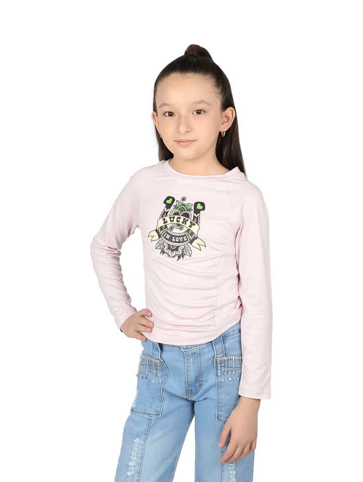 Niña vistiendo blusa rosa palo de manga larga con estampado frontal y pantalones de mezclilla azules.