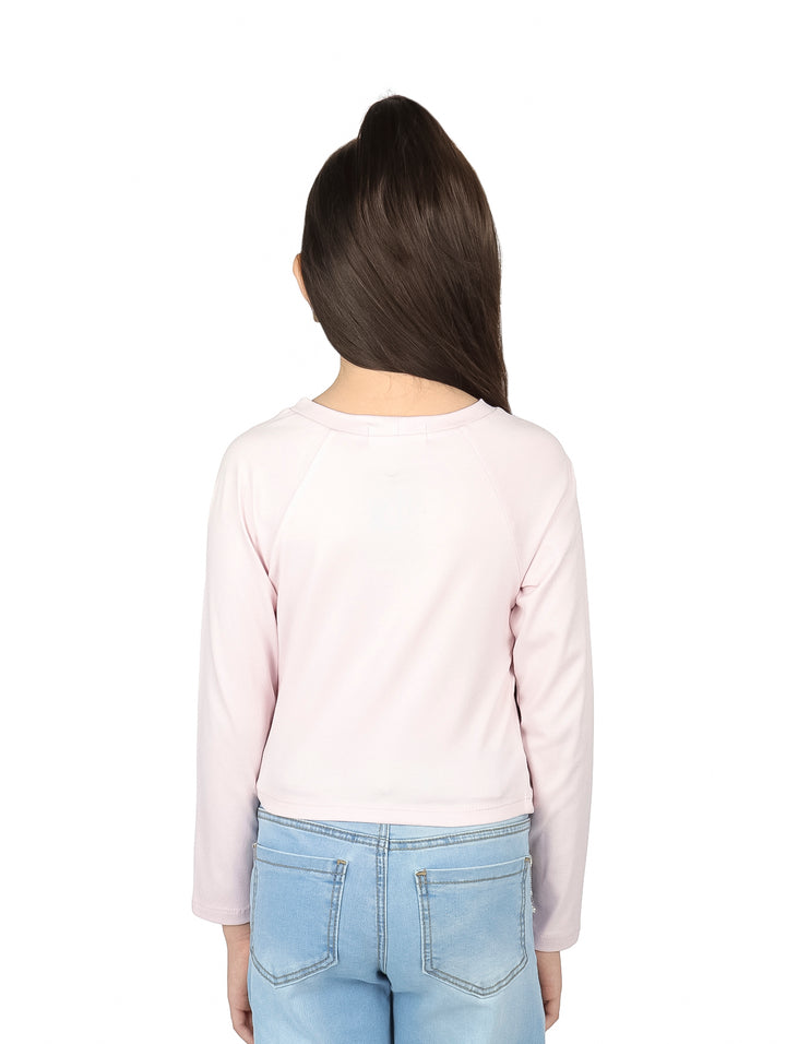 Niña vistiendo blusa rosa palo de manga larga con estampado frontal y pantalones de mezclilla azules.