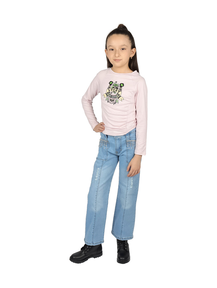 Niña vistiendo blusa rosa palo de manga larga con estampado frontal y pantalones de mezclilla azules.