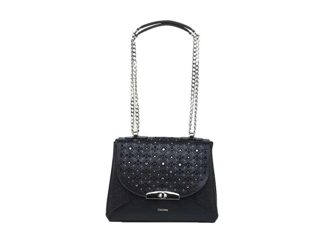 Bolso de cuero negro con correa de cadena plateada y detalles perforados en la solapa.