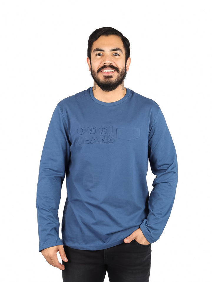 Hombre usando una playera de manga larga color petroleo con logotipo OGGI Jeans en el pecho.