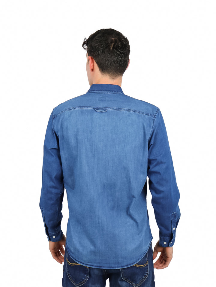 Hombre vistiendo una camisa de mezclilla azul de manga larga con corte slim fit.