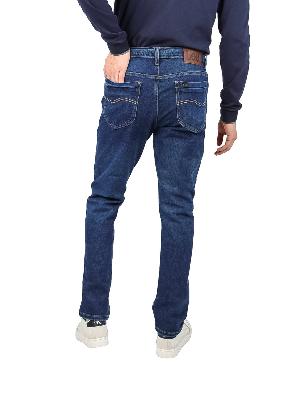 Hombre vistiendo pantalones LEE 112 slim fit en color azul stone con calzado blanco.