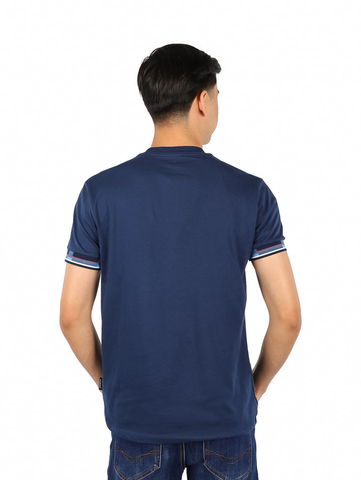 Hombre vistiendo playera azul marino con estampado en el pecho y detalles de rayas en las mangas.