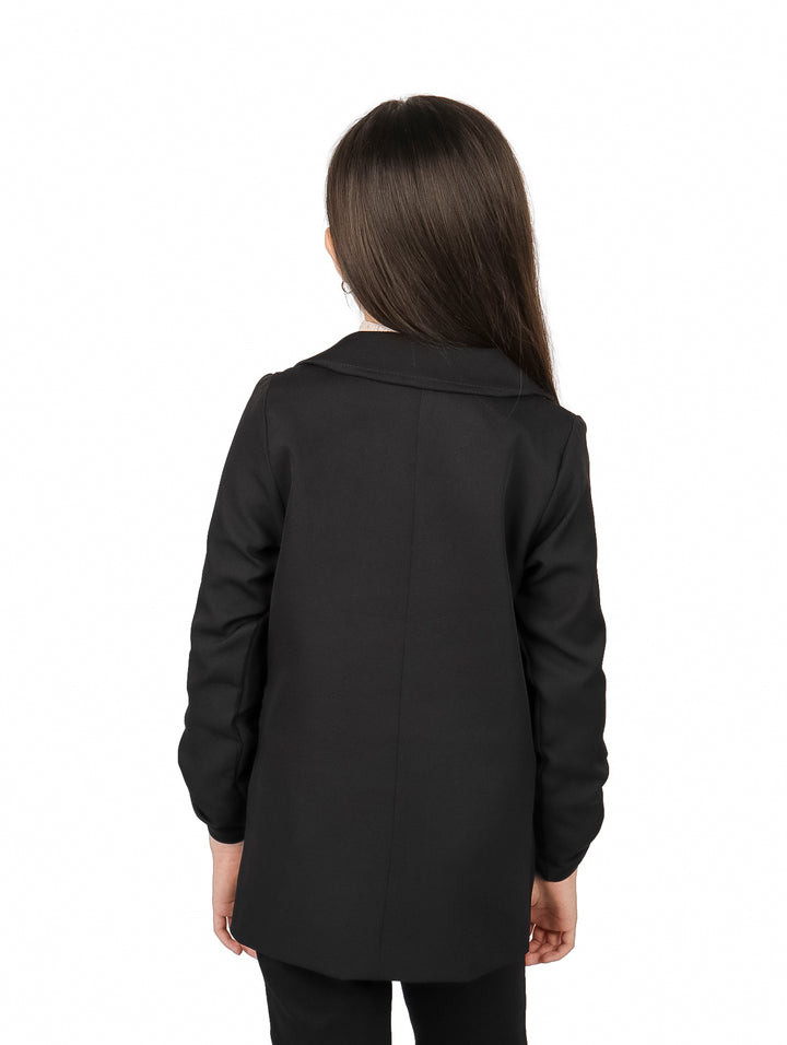 Niña vistiendo un saco negro elegante sobre un suéter beige.