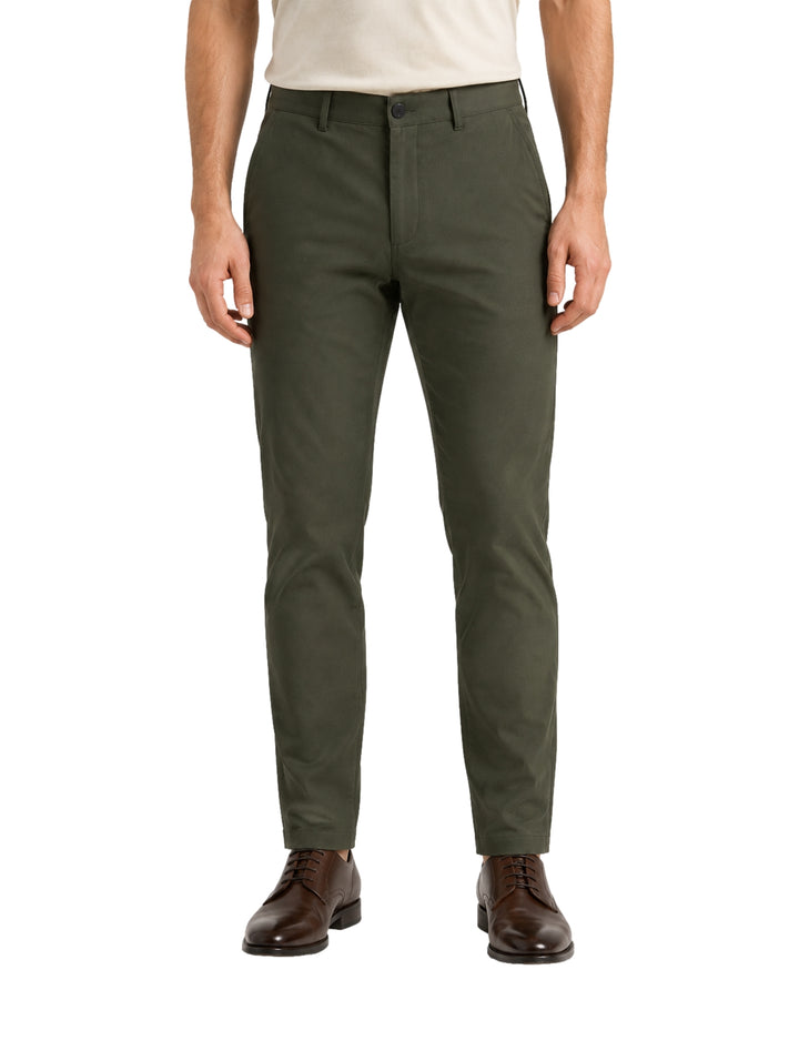 Hombre vistiendo un pantalón color verde oliva de corte slim fit y zapatos cafés.